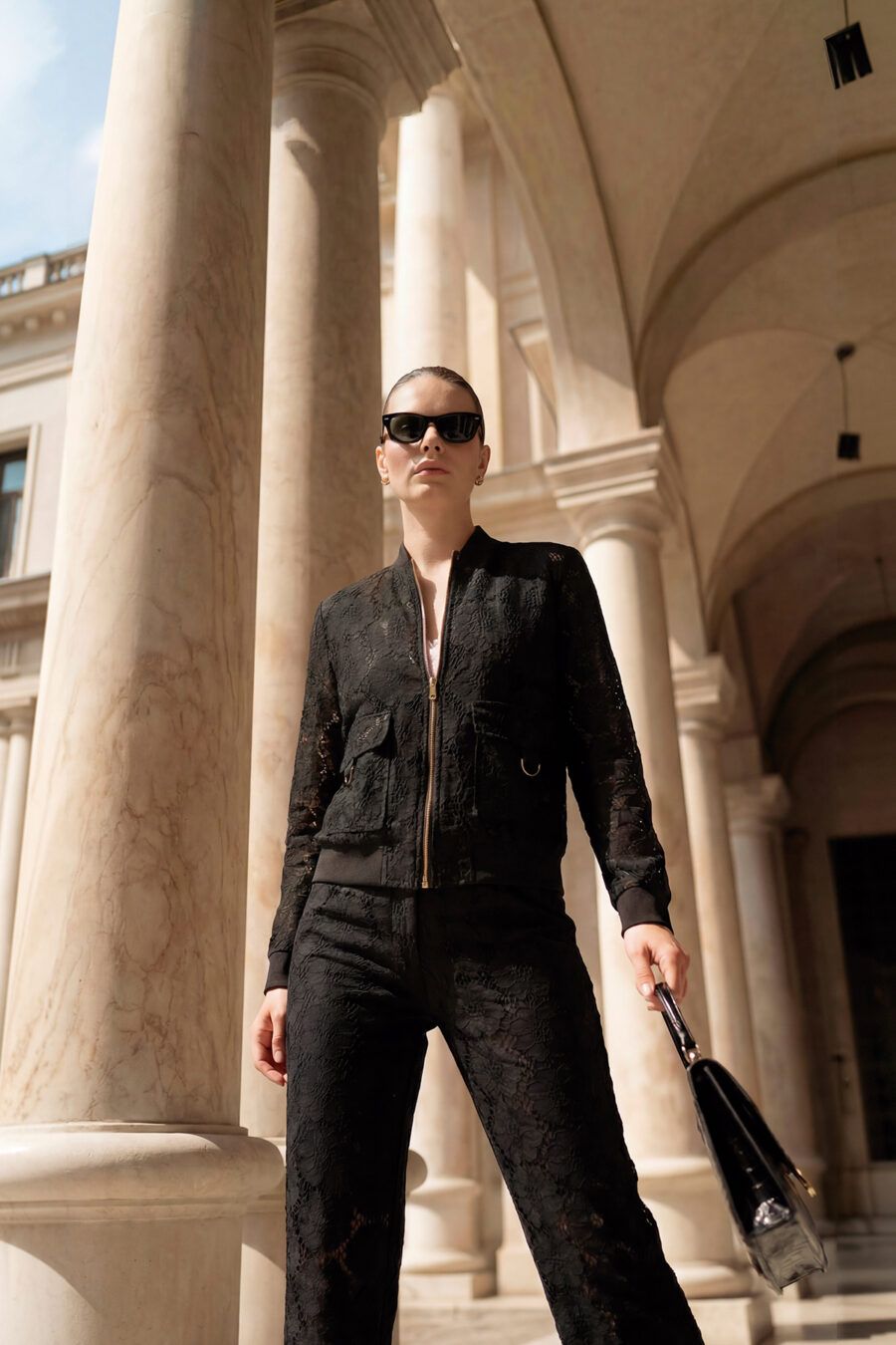 Cazadora tipo bomber confeccionada en un delicado encaje floral negro con sutiles transparencias. Presenta cierre frontal de cremallera dorada, bolsillos de plastrón con solapa y acabados elásticos en puños y cintura, combinando un patrón deportivo con un tejido de máxima sofisticación