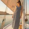 Vestido largo de silueta fluida con un elegante diseño de rayas verticales y horizontales en contraste marino y blanco. Presenta escote en "V" y un corte asimétrico en el bajo que aporta un movimiento sofisticado, ideal para looks de verano con un toque náutico.